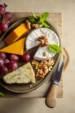 Assortment of gourmet cheese, grapes and nuts on rustic board top view