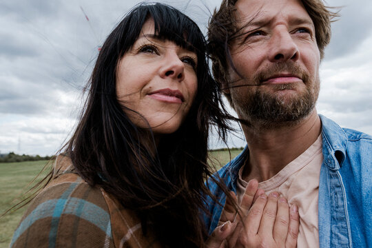 Couple standing hand in hand outdoors on a windy day with wind turbines