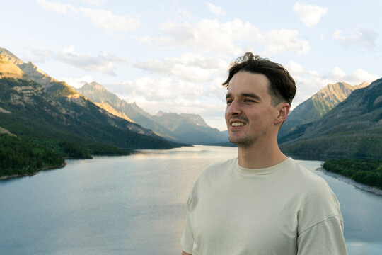 A smiling man in a neutral tee enjoys a lakeside mountain vista at twilight.