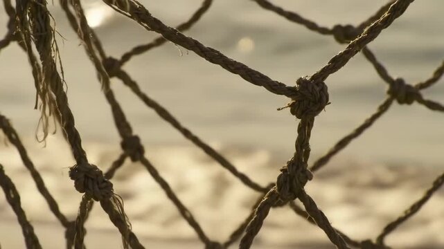 Close-up view of a rough rope net against a blurred ocean backdrop.