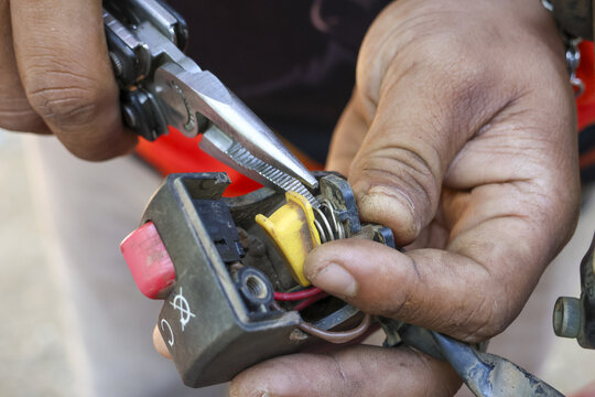 Close up of mechanic hand performing repair on motorcycle switch. skilled technician fixing an electrical wire with pliers during focused vehicle maintenance - Powered by Adobe