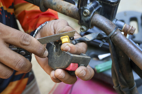 Focused mechanic hand repairing motorcycle lock. Closeup of manual working with tool for vehicle maintenance shows concentration and diligence in workshop