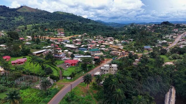 Aerial view of a powerful waterfall cascading amidst the lush greenery, contrasting with the town's buildings, Bafang, West Region, Cameroon.