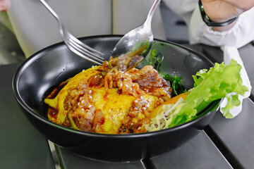 Close-up shot of hands using cutlery to enjoy a portion of Chiffon Egg Bulgogi (Omurice) at a restaurant table. Korean food and lifestyle