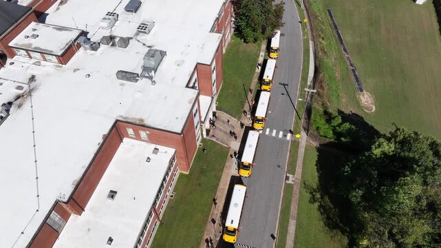 Aerial top down rising shot showing row of traditional parking yellow school buses in summer. People and pupils entering public transport after school. Virginia,USA.