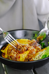 Close-up shot of hands using cutlery to enjoy a portion of Chiffon Egg Bulgogi (Omurice) at a restaurant table. Korean food and lifestyle