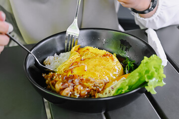 Close-up shot of hands using cutlery to enjoy a portion of Chiffon Egg Bulgogi (Omurice) at a restaurant table. Korean food and lifestyle