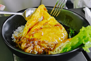 Close-up shot of hands using cutlery to enjoy a portion of Chiffon Egg Bulgogi (Omurice) at a restaurant table. Korean food and lifestyle
