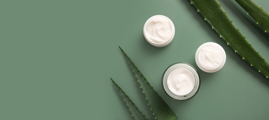Jars of cosmetic cream with aloe vera extract on green background with space for text