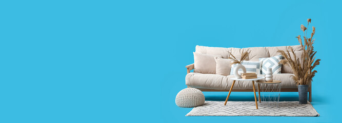 Comfortable white sofa, coffee table and pampas grass on blue background