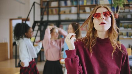 Friends are gathered in a classroom setting, chatting and laughing. One red-haired student is blowing a bubble with gum, while others style their hair and smile. - Powered by Adobe
