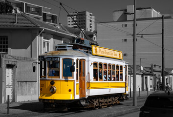 Historic tram “Line 1“ in the Portuguese port city of Porto. The old yellow electric railcars are a popular tourist attraction. Colorful vintage public transport vehicle on black and white background.