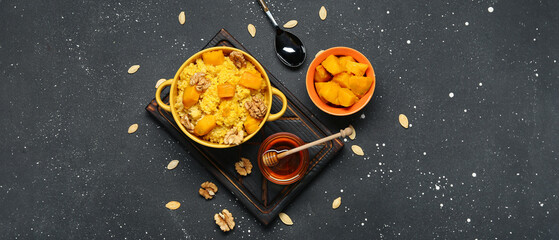 Pot of tasty millet porridge with pumpkin and ingredients on black background