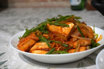 Spicy stir-fried tofu with onions and green onions in a white bowl