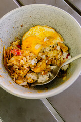 Top-down view of Nasi Ayam Cangu, an Indonesian dish with rice, spiced chicken, and fried egg, mixed and halfway eaten, ready to be enjoyed