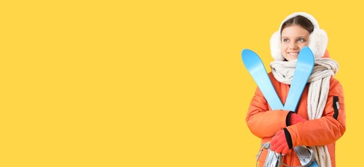 Happy little girl with skis on yellow background with space for text