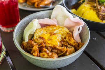 Close-up of Nasi Ayam Cangu, an Indonesian dish featuring rice topped with savory spiced chicken, fried egg, and pink prawn crackers