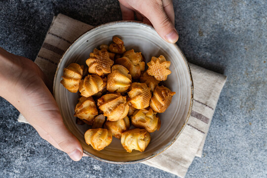 Homemade caramel profiteroles in ceramic bowl held by hands