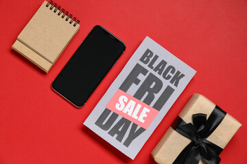Black Friday sale greeting card with mobile phone, notepad and gift box on red background