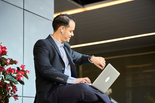Latin businessman multitasking with laptop and smartwatch outdoors - Powered by Adobe