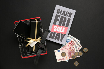 Obraz premium Greeting card with text BLACK FRIDAY SALE, shopping basket, gifts, credit cards and money on dark background