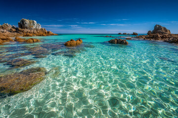 Crystal clear turquoise water gently flowing around rugged rocky formations under a brilliant blue sky in a serene coastal landscape at midday