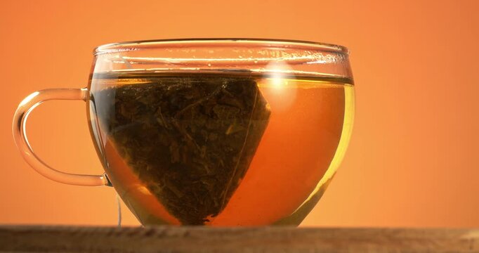 Transparent cup with tea and tea bag close-up footage on a rotating table.