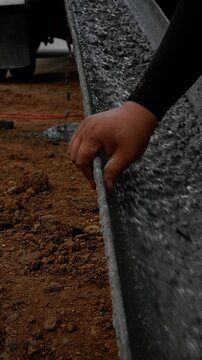 A dynamic, close-up shot captures the process of pouring fresh, wet concrete into a makeshift formwork channel on a construction site. The thick, viscous mixture is rapidly flowing, creating a motion 