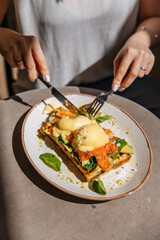 Close-up photo of a girl cutting toast with eggs benedict, red fish and spinach. Top view on the table