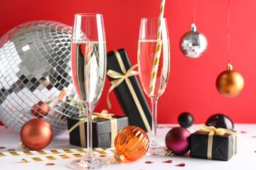 Composition with glasses of champagne, Christmas gifts and decorations against red background