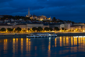 Blue hour view of boat on the Danube River, the coastline and the illuminated Buda Castle complex,...