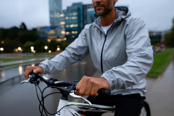 Fototapeta premium A thief man rides a bicycle through the rain-soaked urban streets, embodying determination and resilience against the weather's challenges in a cityscape.