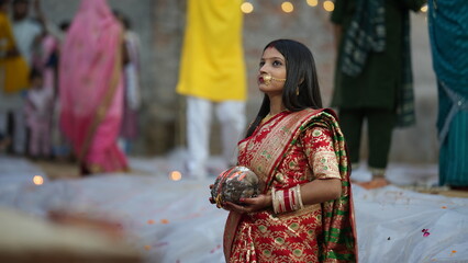 Newlywed woman dressed in red saree offering coconut during Chhath Puja at sunrise, showcasing Indian faith, devotion, and cultural elegance.