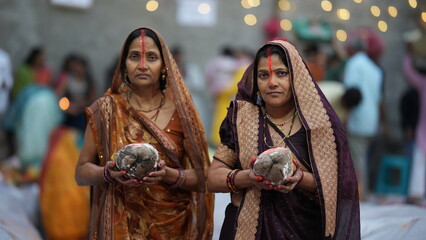 Women holding coconuts as offerings during Chhath Puja sunrise prayers, symbolizing devotion, purity, and deep spiritual faith in Indian culture.