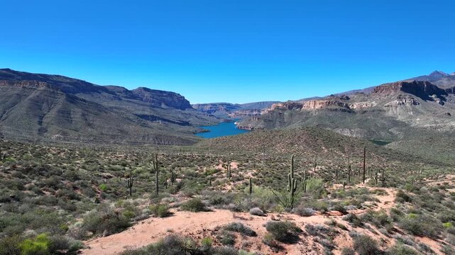 Aerial view of the Apache Trail winding through the rugged terrain towards the serene blue waters of Canyon Lake under a clear sky, Apache Junction, Arizona, United States.