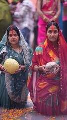Two women offering coconuts and Fruits in holy water during Chhath Puja, expressing devotion and spirituality in early morning light.