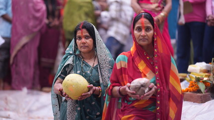 Women standing in holy water holding Fruits and coconuts during Chhath Puja sunrise ritual, symbolizing faith, purity, and devotion.