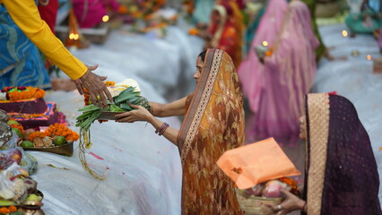 A devoted woman performs Chhath Puja rituals near water with offerings in hand, wearing a traditional saree during early morning prayers.