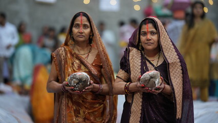 Women offering prayers during Chhath Puja at sunrise, holding offerings, reflecting devotion, peace, and cultural grace.