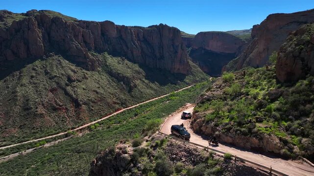 Aerial view of a car navigating a winding dirt road through Fish Creek Hill, embraced by rugged mountains under a vast blue sky, Apache Junction, Arizona, United States.