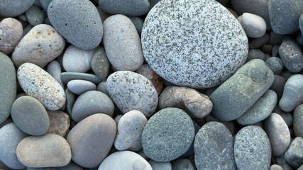 Close-up of smooth natural river stones and pebbles in various shades of gray, white, and speckled patterns, weathered and polished textures, arranged organically