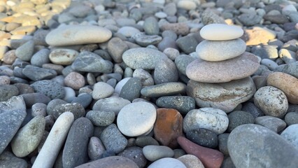 Balanced cairn of smooth rounded stones atop a pebble beach with natural assortment of various shapes, sizes, and colors under soft sunlight