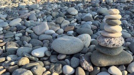 Balanced cairn of smooth rounded stones atop a pebble beach with natural assortment of various shapes, sizes, and colors under soft sunlight