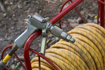 Powerful industrial spray gun nozzle and yellow high pressure hose on red reel. Metal equipment for...