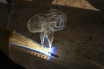 Mysterious smoke from smoldering incense stick with light beam causing spectrum refraction. An...