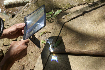 Curious science experiment using magnifying glass lens focusing sunlight. hand holds lens creating intense heat and solar energy, slowly burning green leaf