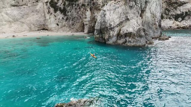 Agrilias, Greece - 16 October 2025: Aerial view of a person kayaking on the turquoise water near a beach and rocky cliffs with caves.