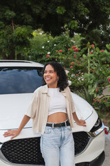 Young woman smiling leaning on white car outdoors