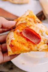 Close-up of a hand lifting a delicious pizza slice with a massive cheese pull. Perfect for conveying comfort food, indulgence, and Italian dining