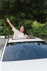 Woman enjoying road trip freedom waving from sunroof